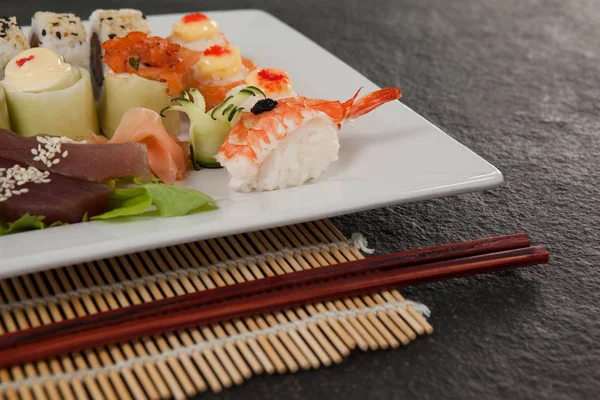 Conjunto de sushi sortido servido com pauzinhos em placa branca no tapete de sushi — Fotografia de Stock