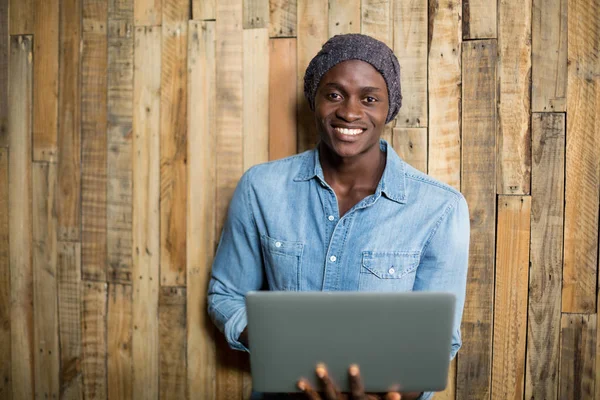 Uomo sorridente utilizzando il computer portatile contro parete di legno — Foto Stock