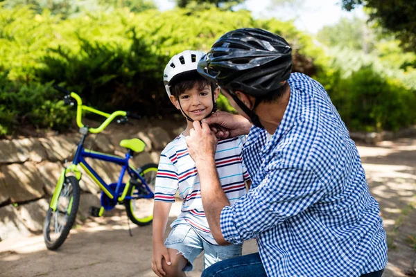 Padre ayudando a hijo en el uso de casco de bicicleta en el parque —  Fotos de Stock