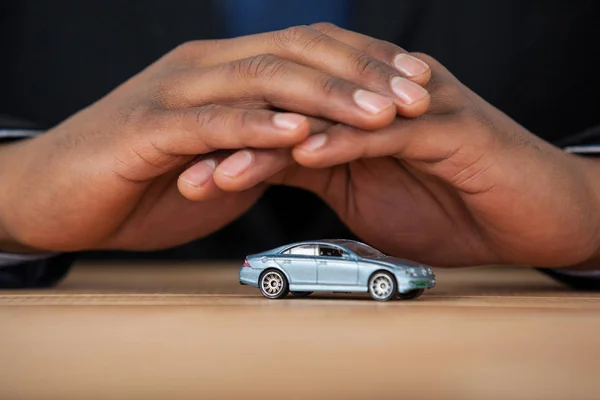 Homme d'affaires protégeant la voiture jouet avec les mains — Photo