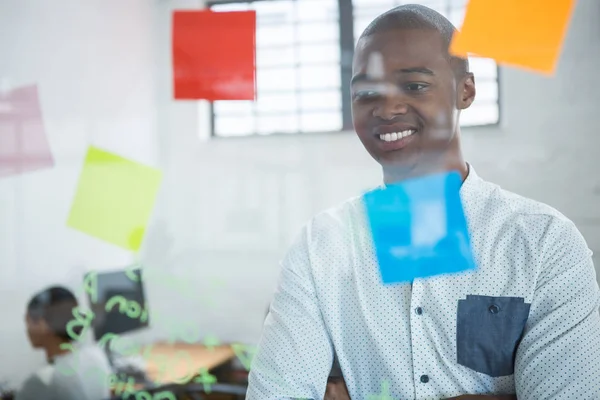 Smiling businessman reading sticky notes on glass — Stock Photo, Image