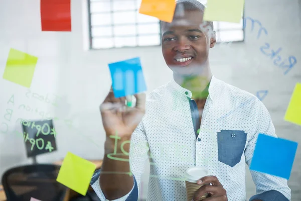 Hombre de negocios sonriente escribiendo en notas adhesivas — Foto de Stock
