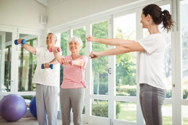 Female trainer assisting senior couple in performing exercise — Stock Photo, Image