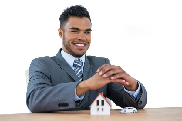 Smiling businessman protecting house model and car with hands — Stock Photo, Image