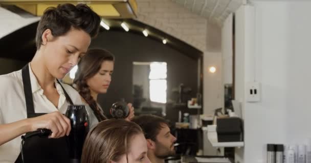 Dois cabeleireiro golpe secando seu cabelo cliente — Vídeo de Stock