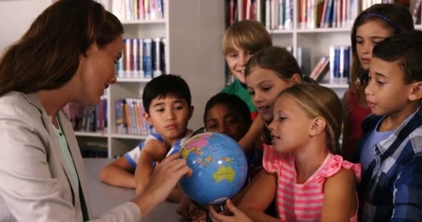 Profesor ayudando a los niños de la escuela en la lectura globo en la biblioteca — Vídeos de Stock