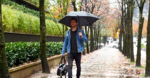 Homme tenant un parapluie et marchant dans la rue — Video