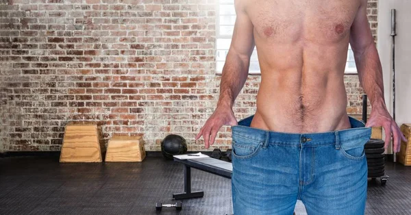 Fitness man Torso wearing a huge jeans in a gym to show how he lost weight
