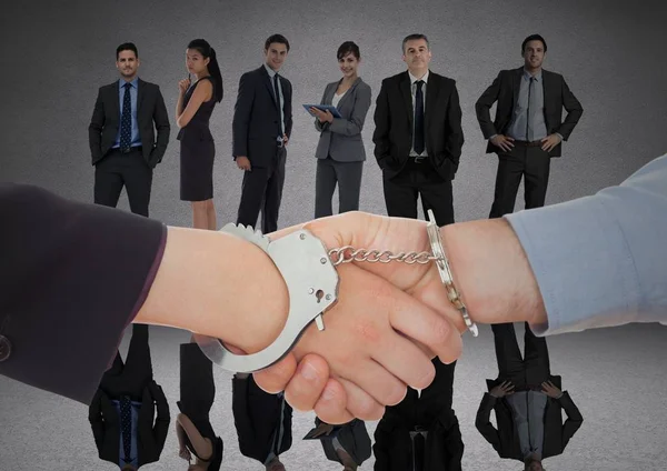 Рукопожатие с наручниками перед деловыми людьми в серой комнате — стоковое фото