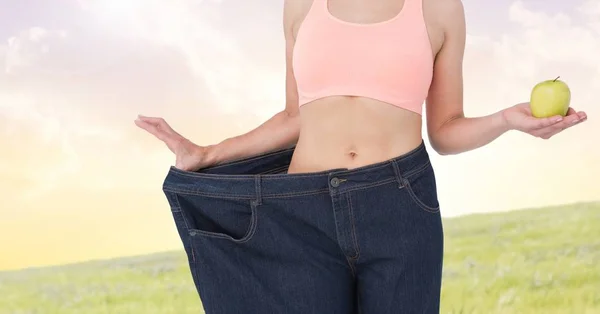 健身女人躯干穿着巨大的裤子，拿着一个苹果，向她展示节食来减肥 — 图库照片