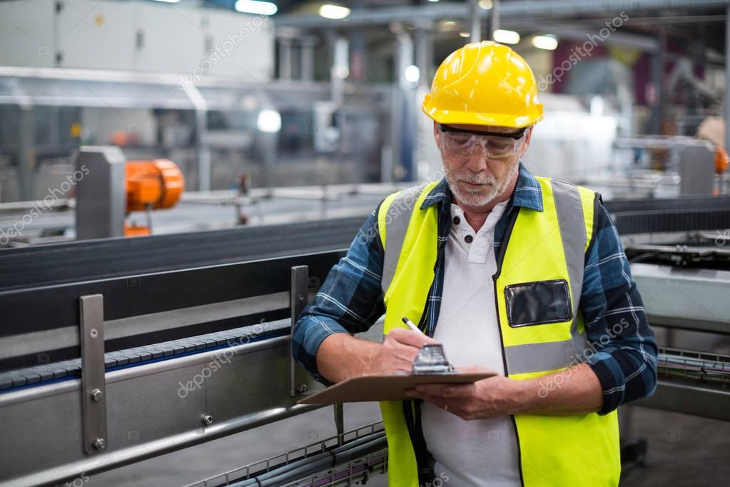 Male factory worker maintaining record on clipboard