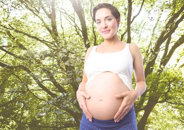 Беременная женщина, стоящая против зелени — стоковое фото