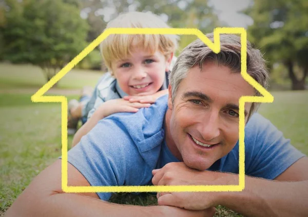 Dad and son laying in the park against house outline in background — Stock Photo, Image