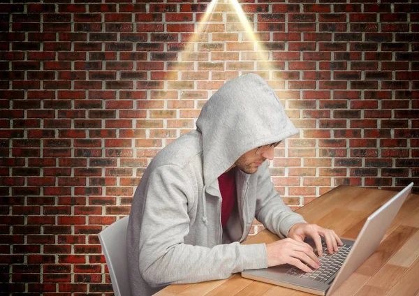 Muž s kapucí sedí proti cihlové zdi a pomocí přenosného počítače — Stock fotografie