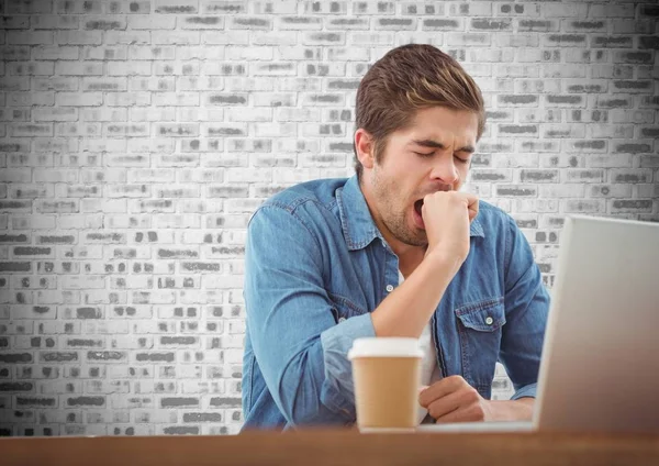 Чоловік позіхання під час використання ноутбука в офісі на фоні цегляної стіни — стокове фото