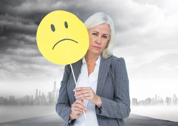 Empresaria sosteniendo una cara triste delante de su cara con nubes de lluvia en el fondo — Foto de Stock