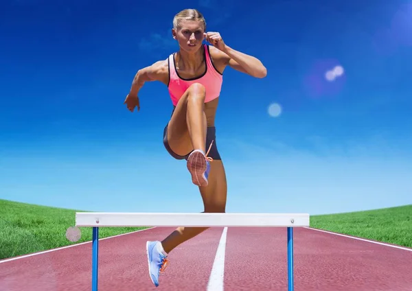 Female athlete jumping over hurdle on race track — Stock Photo, Image