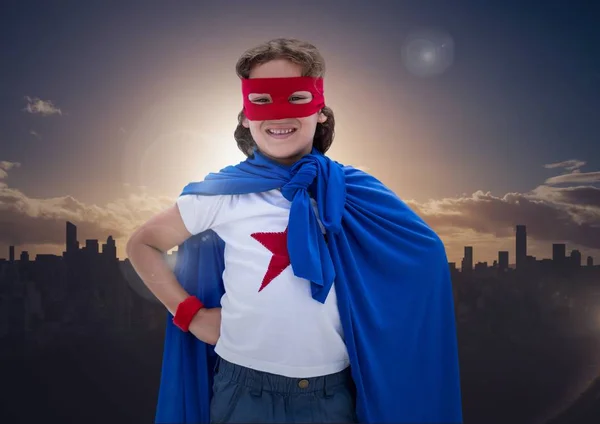 Jongen in superheld kostuum permanent met zijn handen op zijn heupen tegen stadsgezicht achtergrond — Stockfoto