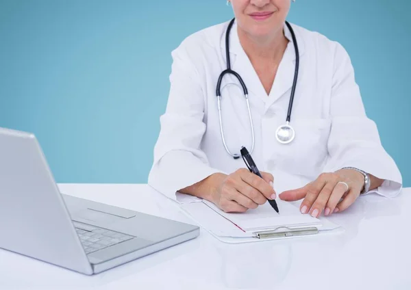 Female doctor sitting at desk with laptop and writing on clipboard — Stock Photo, Image