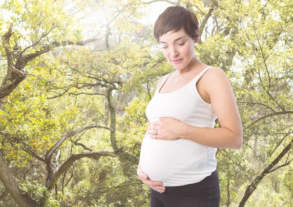 Беременная женщина, стоящая против зелени — стоковое фото