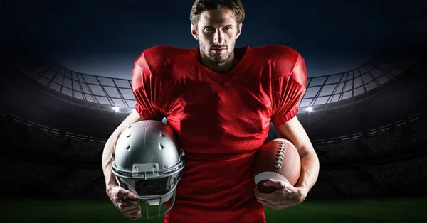 Jogador de futebol americano segurando bola de rugby e capacete contra estádio no fundo — Fotografia de Stock