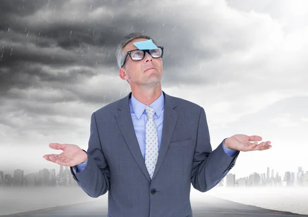 Uomo d'affari confuso con una nota appiccicosa attaccata sulla fronte contro il cielo tempestoso sullo sfondo — Foto Stock