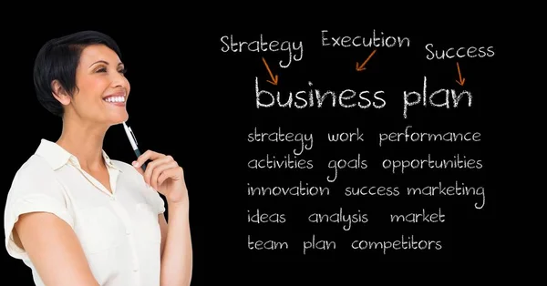 Empresária sorridente segurando caneta e de pé contra quadro negro com termos de negócio — Fotografia de Stock