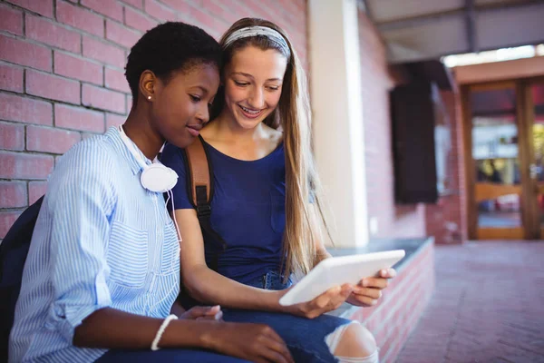 Tuğla duvara oturan ve tablet kullanarak kız öğrenciler — Stok fotoğraf
