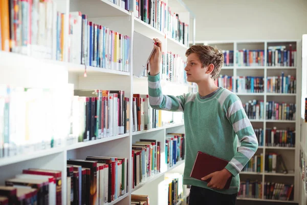 Schoolboy selecionando livro na biblioteca — Fotografia de Stock