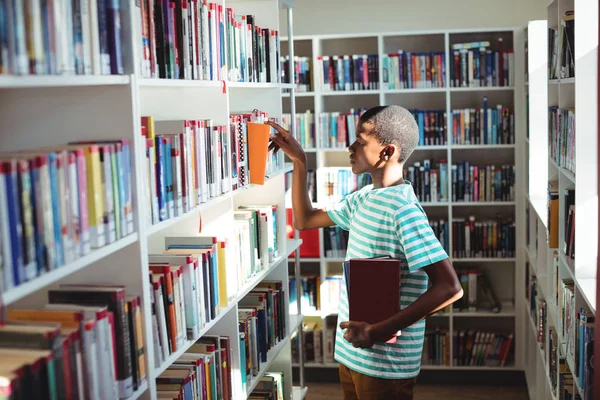 Schooljongen selecteren boek in bibliotheek — Stockfoto