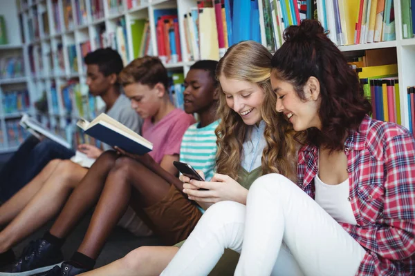 Studenten met behulp van mobiele telefoon in bibliotheek — Stockfoto