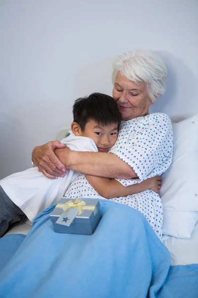 Pojken att ge en kram till senior patient på säng — Stockfoto