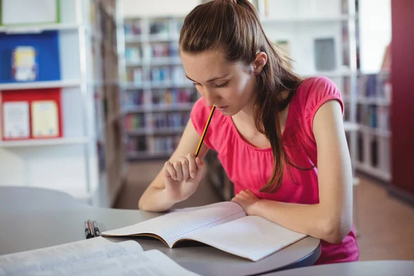 Skolflicka gör läxor i bibliotek — Stockfoto