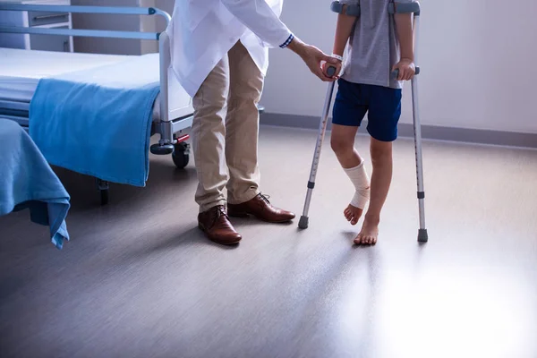 Médico assistindo menino ferido para andar com muletas — Fotografia de Stock