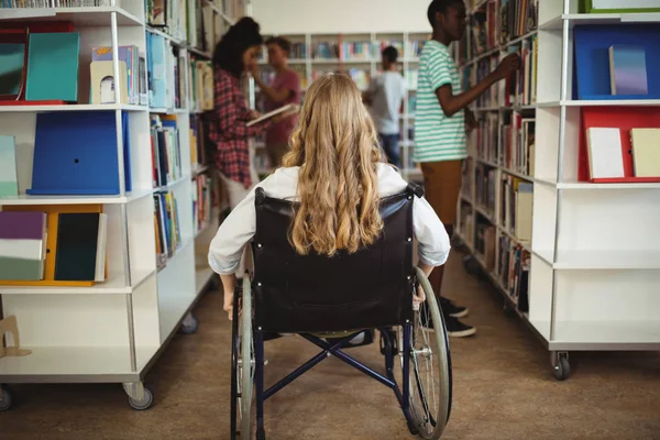 Menina com deficiência em cadeira de rodas na biblioteca — Fotografia de Stock