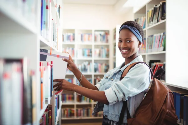 Schoolgirl selecting book from book shelf in library — Stock Photo, Image