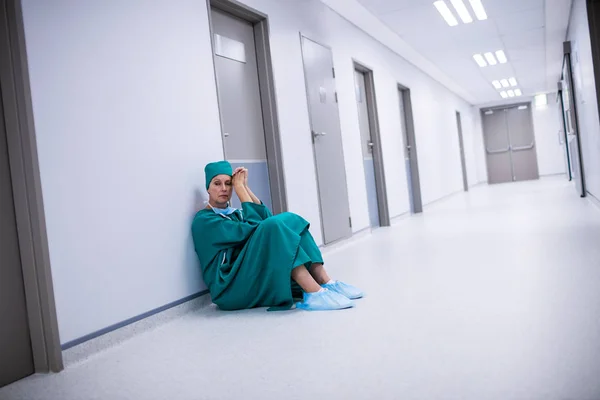 Напряженная женщина-хирург сидит в коридоре — стоковое фото