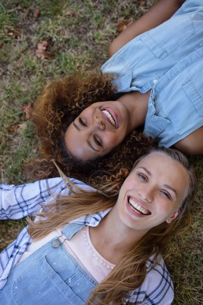 Amigos femininos deitados juntos na grama no parque — Fotografia de Stock