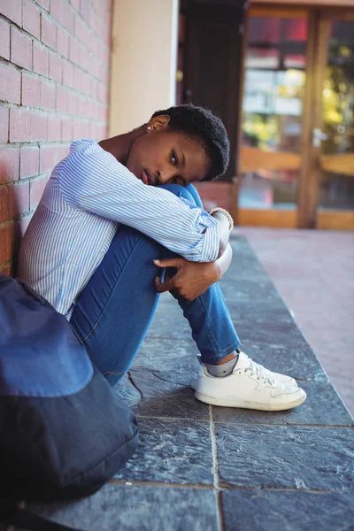 Sad schoolgirl sitting against brick wall — Stock Photo, Image