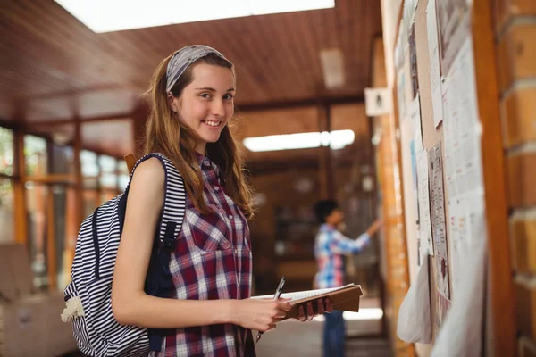 Schoolgirl standing with book near notice board — Stock Photo, Image