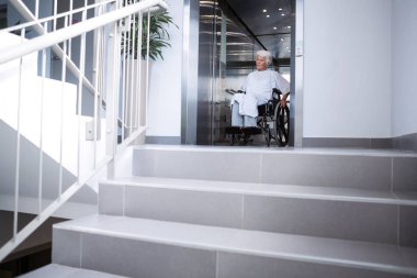 Disabled senior patient on wheelchair in lift clipart