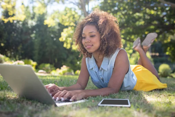Kvinna liggande på gräs och använder bärbar dator — Stockfoto