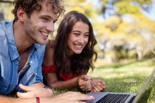 Coppia sdraiata sull'erba e utilizzando il computer portatile — Foto Stock