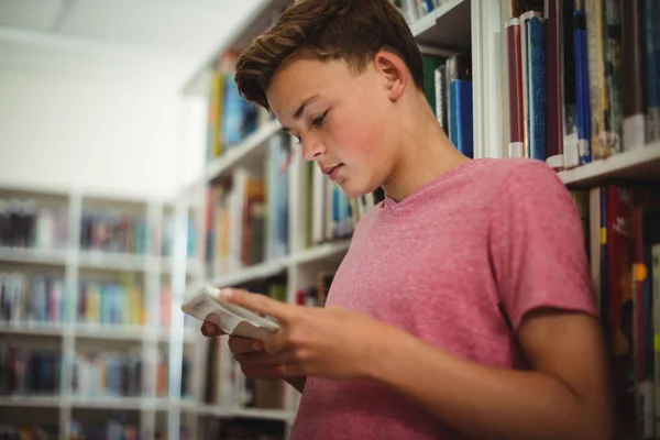 Schooljongen via digitale tablet in bibliotheek — Stockfoto