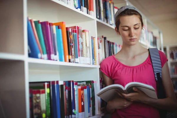 Attentive schoolgirl reading book in library — Stock Photo, Image