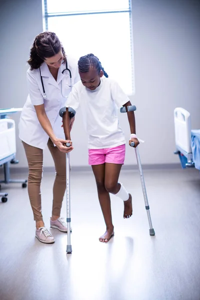 Γυναίκα γιατρό που βοηθά το κορίτσι να περπατούν με δεκανίκια — Φωτογραφία Αρχείου