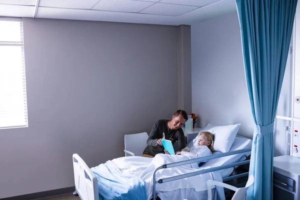 Dziewczyna na szpitalnym łóżku czytając książkę z ojcem — Zdjęcie stockowe