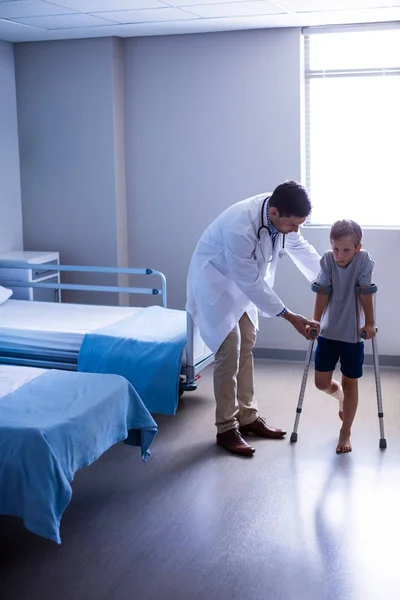 Médico assistindo menino ferido para andar com muletas — Fotografia de Stock
