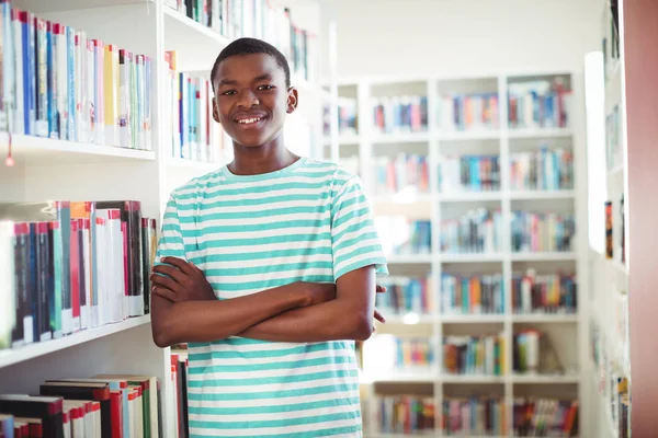Школьник, стоящий со скрещенными руками в библиотеке — стоковое фото