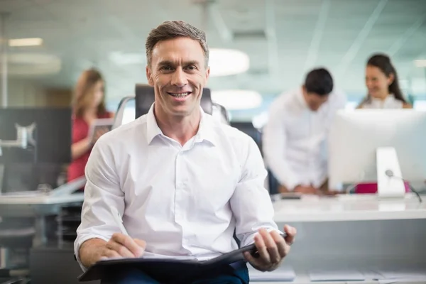 Business executive sitting on chair and writing on clipboard — Stock Photo, Image